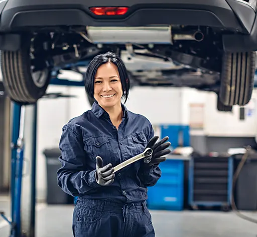 A female auto mechanic holding a spanner while in front of a suspended car