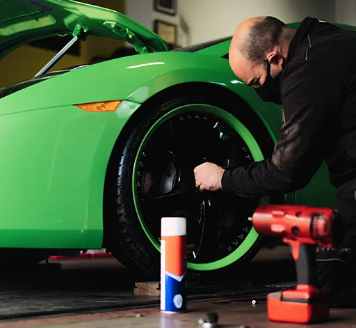 A professional auto mechanic working on the wheels of a high-end sports car