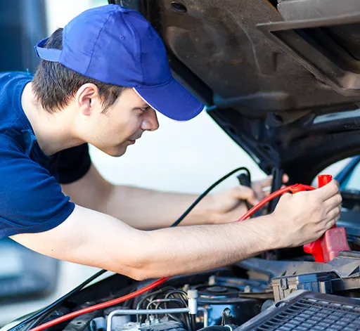 An auto mechanic attaching jumper cables to a car's battery
