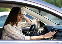 A female driver wiping her forehead because of her car's broken airconditioning unit