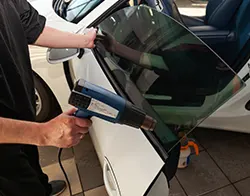 An auto mechanic using a blower on freshly installed car window tint