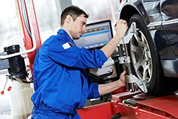 A car mechanic using a caster/camber gauge to check on a suspended car's wheel alignment