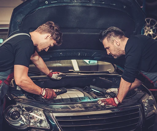 Two auto mechanics checking under the hood of a car