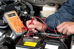 A mechanic checking the voltage level in a car battery using a voltmeter